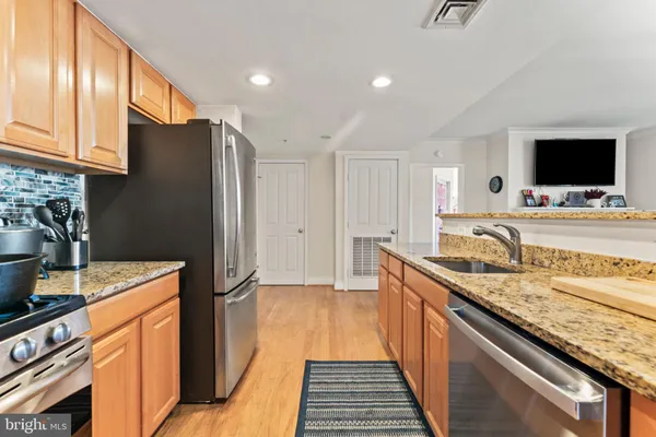 a kitchen with stainless steel appliances granite countertop a refrigerator a stove and a sink with wooden floor