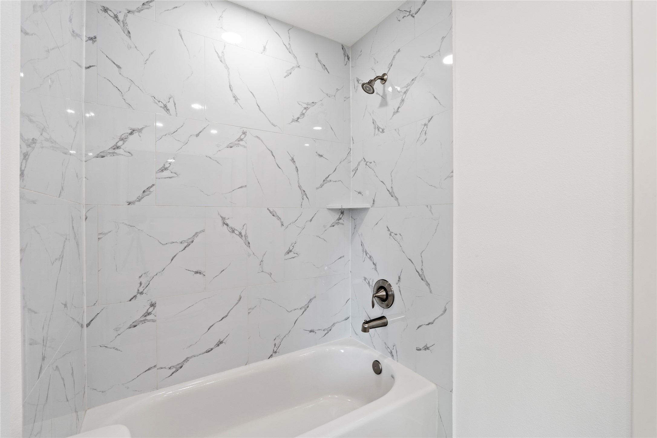 5023 Redstart Street Houston, TX 77035 - Photo 30 of 34 The shower-tub combination is elevated by floor-to-ceiling marble-style tile with delicate grey veining and polished chrome fixtures.