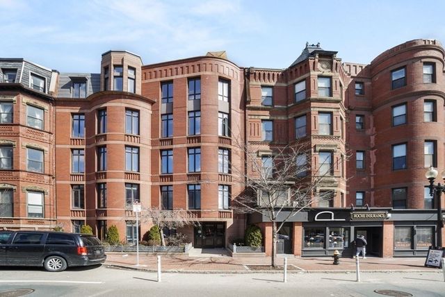 a front view of a building with lot of cars and trees