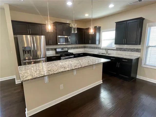 a large kitchen with stainless steel appliances a large counter top a stove a sink a refrigerator and a wooden floor