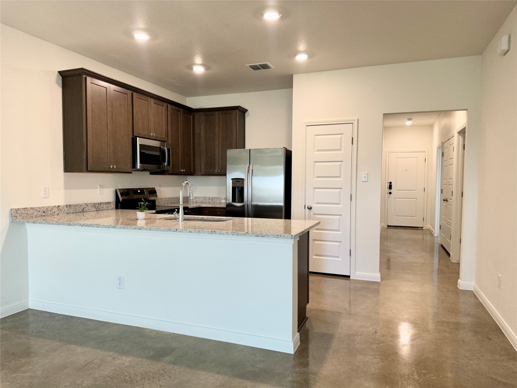 2913 Quail Rdg Lane, Unit A Temple, TX 76501 - Photo 8 of 19 Kitchen with dark brown cabinets, appliances with stainless steel finishes, light stone countertops, finished concrete floors, and a peninsula