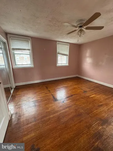 an empty room with wooden floor fan and windows