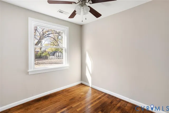 an empty room with wooden floor chandelier fan and windows