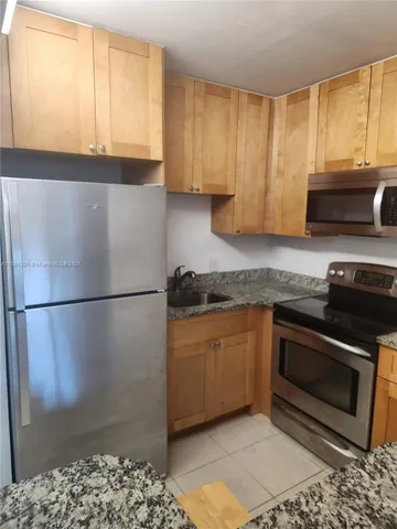 a kitchen with granite countertop a refrigerator a stove a sink and a window