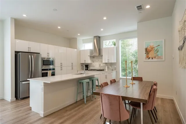 a kitchen with stainless steel appliances a dining table chairs refrigerator and sink