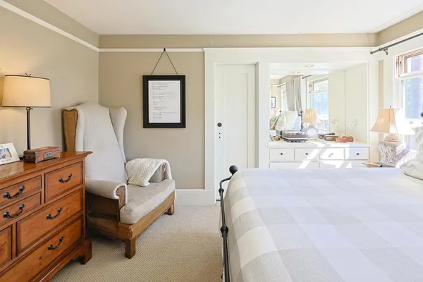 a spacious bedroom with a bed and a lamp on dresser next to a window