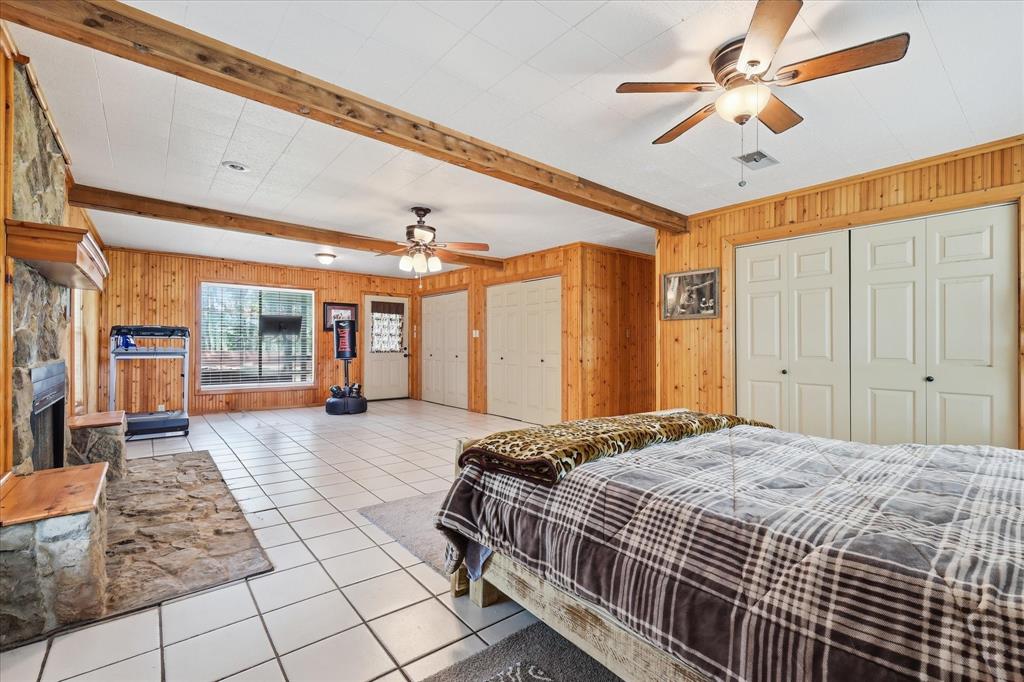 237 Brenda Lane Gainesville, TX 76240 - Photo 19 of 40 Spacious room featuring wood paneling, exposed ceiling beams, a stone fireplace with a wood mantle, white tile flooring, and multiple ceiling fans