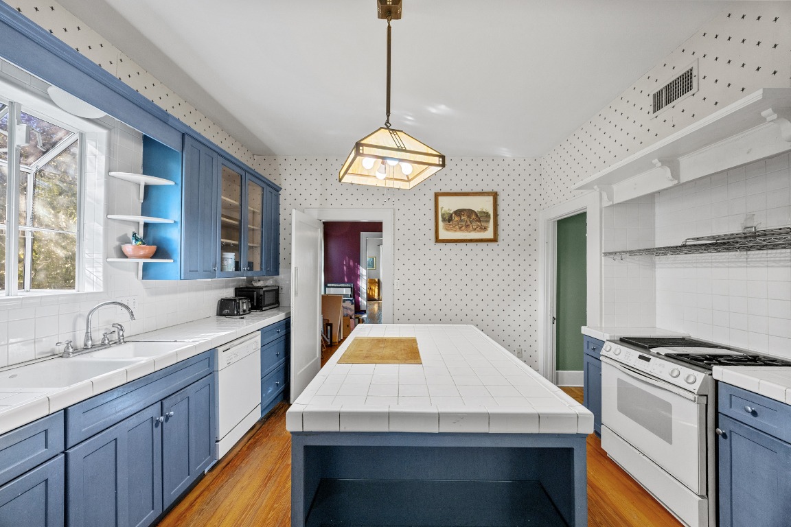 1006 Maple Street Lockhart, TX 78644 - Photo 8 of 32 Kitchen featuring tasteful backsplash, blue cabinets, open shelves, white appliances, and wallpapered walls