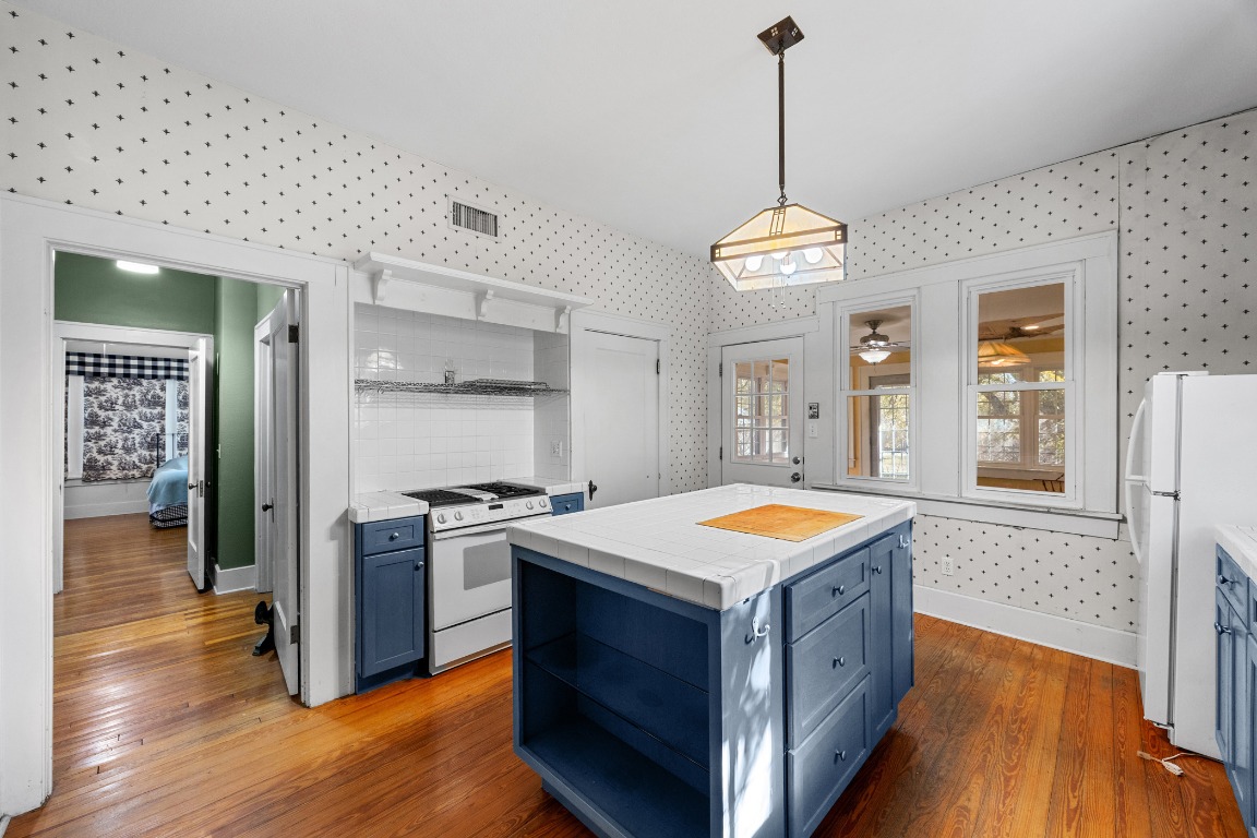 1006 Maple Street Lockhart, TX 78644 - Photo 9 of 32 Kitchen with blue cabinetry, open shelves, tile countertops, white appliances, and wallpapered walls