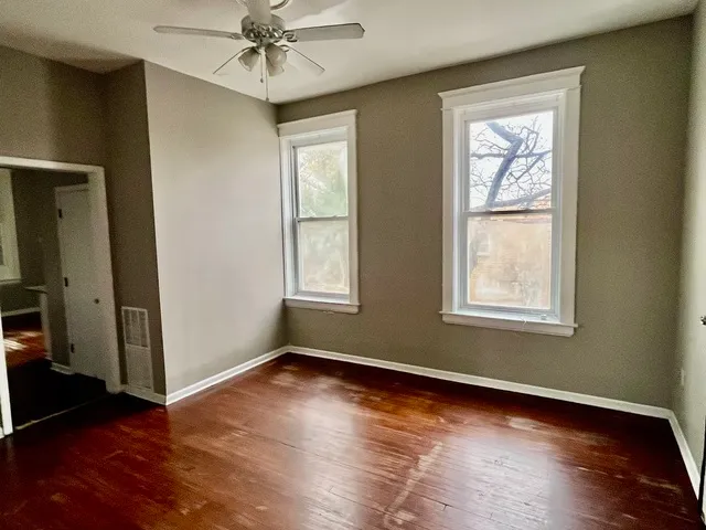 an empty room with wooden floor fan and windows
