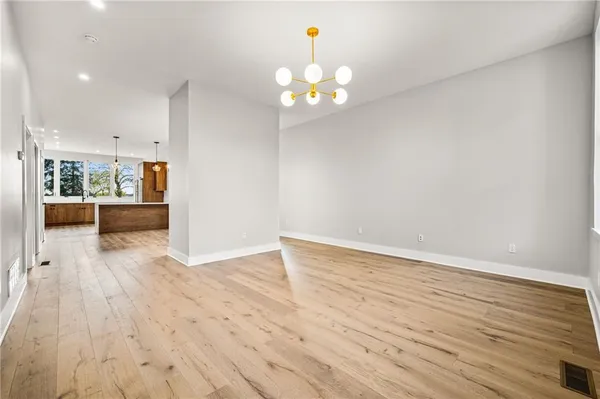 a view of an empty room with wooden floor and a kitchen