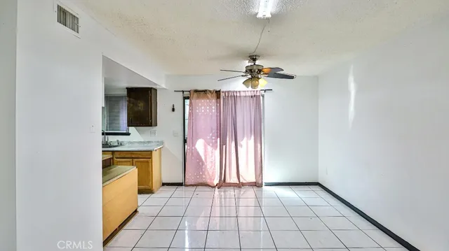 an empty room with chandelier fan and kitchen view