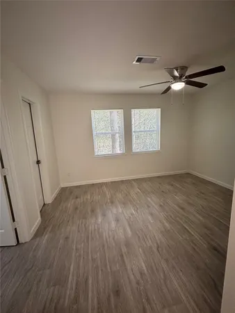 an empty room with wooden floor fan and windows