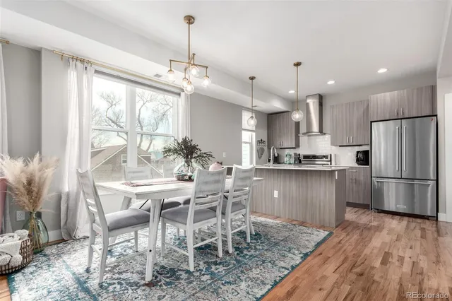 a kitchen with stainless steel appliances granite countertop a refrigerator a oven a sink a dining table and chairs with wooden floor