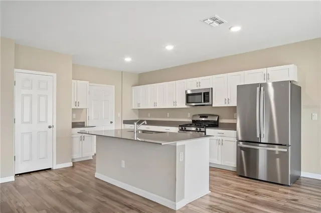 a kitchen with stainless steel appliances white cabinets a sink a stove a refrigerator and white cabinets