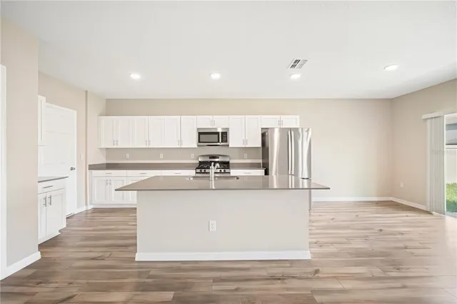 a large kitchen with stainless steel appliances granite countertop a large counter top and a stove with wooden floor