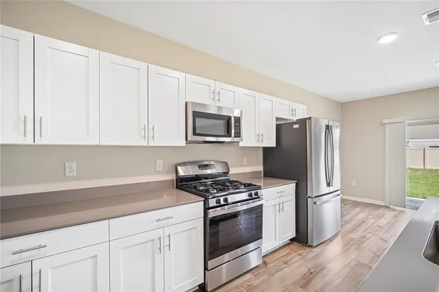 a kitchen with granite countertop white cabinets stainless steel appliances and a wooden floor