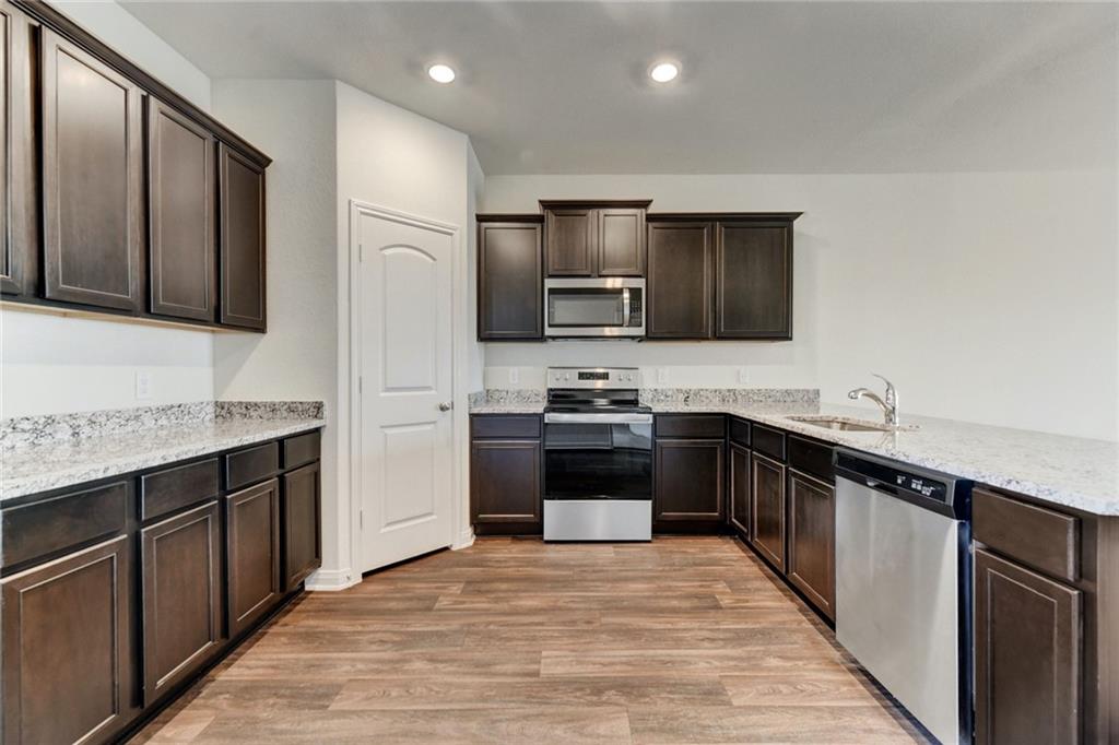 105 Brunswick Lane Jarrell, TX 76537 - Photo 8 of 16 Kitchen with dark wood finish cabinetry, stainless steel appliances, light wood-style floors, a peninsula, and light stone counters