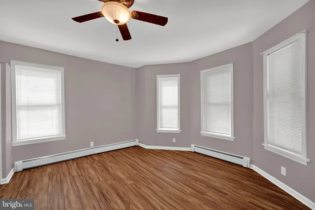 a view of empty room with wooden floor and fan