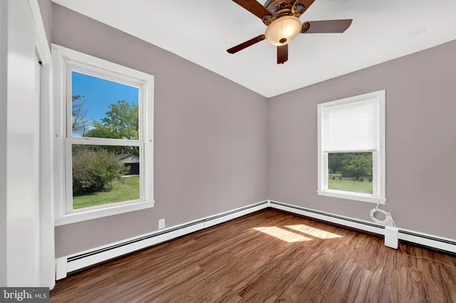 an empty room with wooden floor chandelier fan and windows