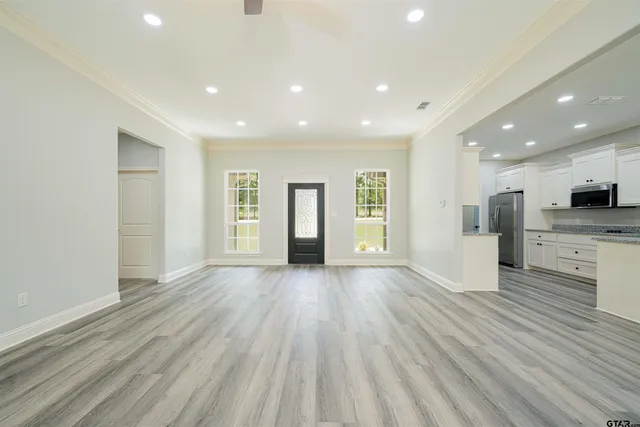 a view of an empty room with wooden floor kitchen view and a window