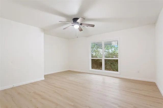 an empty room with wooden floor ceiling fan and windows