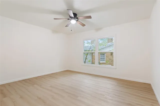 an empty room with wooden floor fan and windows