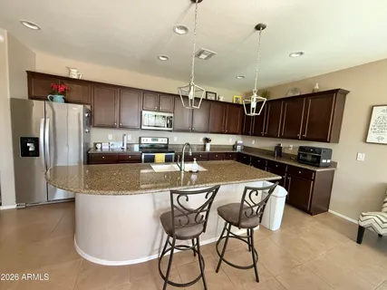 a kitchen with stainless steel appliances granite countertop a refrigerator a stove a sink a dining table and chairs with wooden floor