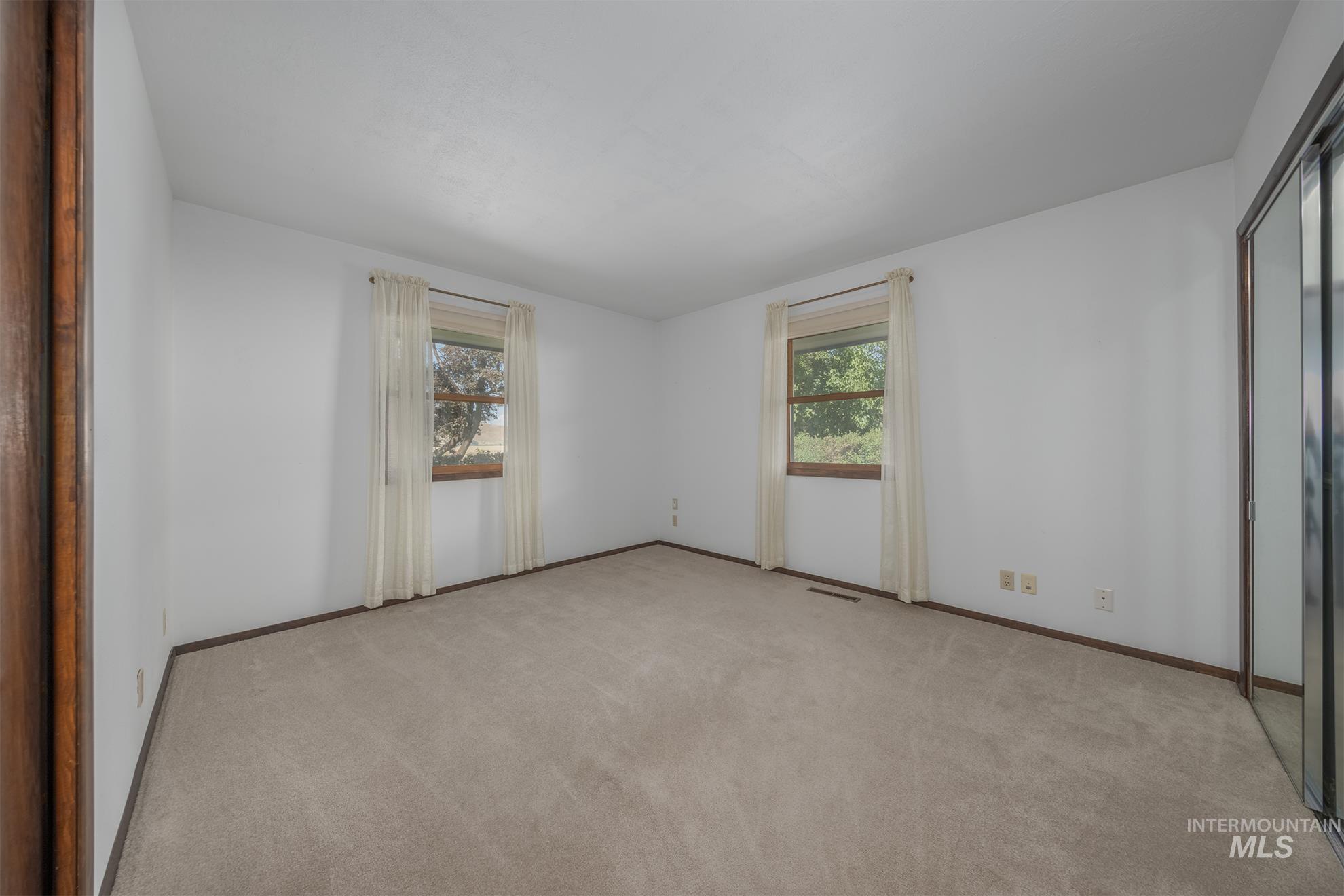 1493 Cove Road Weiser, ID 83672 - Photo 10 of 50 Carpeted room with white walls, two windows featuring wood trim, and a mirrored closet door