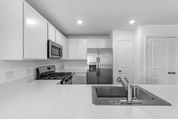 a kitchen with stainless steel appliances kitchen island granite countertop a refrigerator a stove a sink and white cabinets with wooden floor