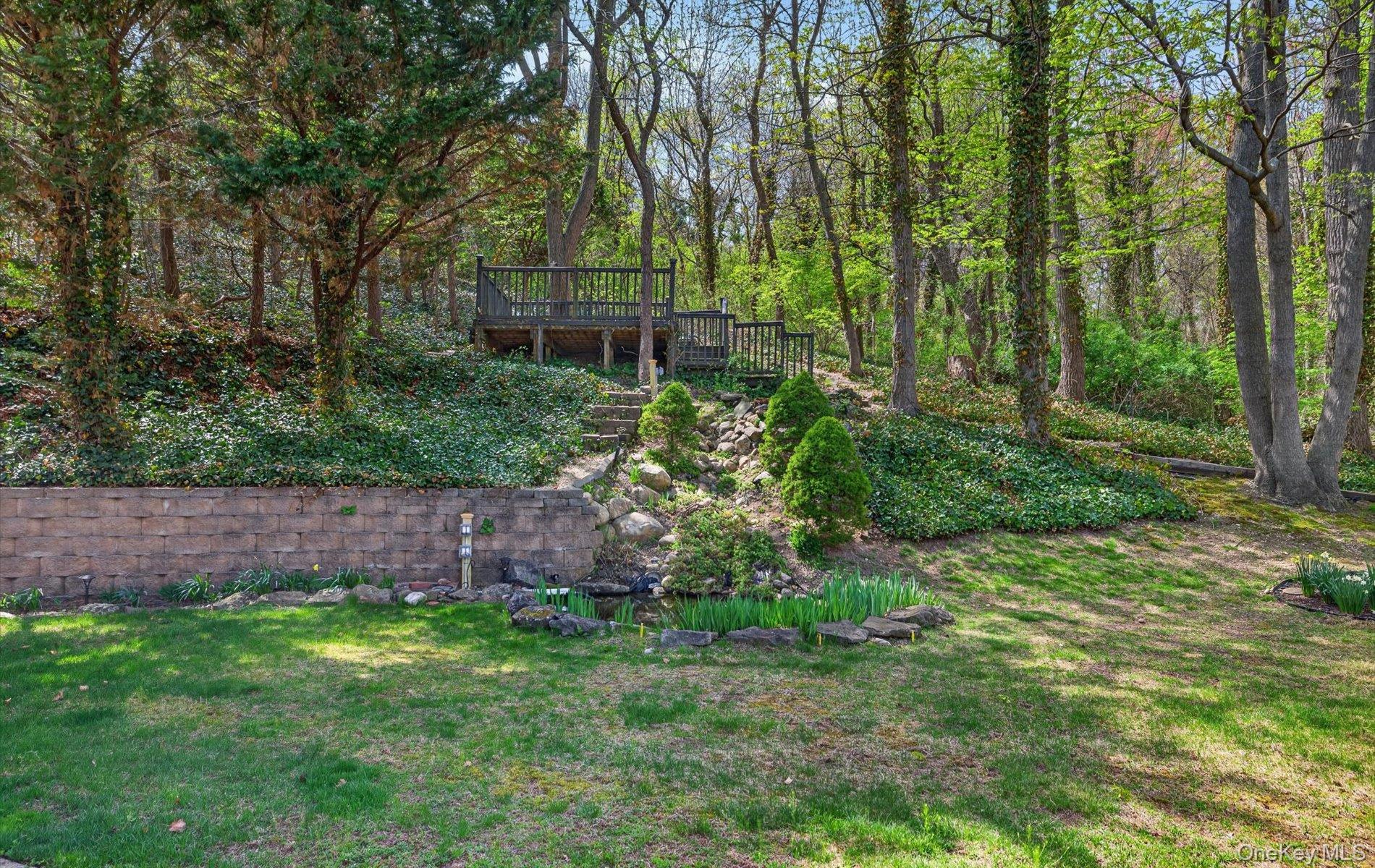 16 East Slope Road Bayville, NY 11709 - Photo 42 of 48 Terraced backyard featuring a wooden deck, stone retaining wall, mature trees, and established ground cover