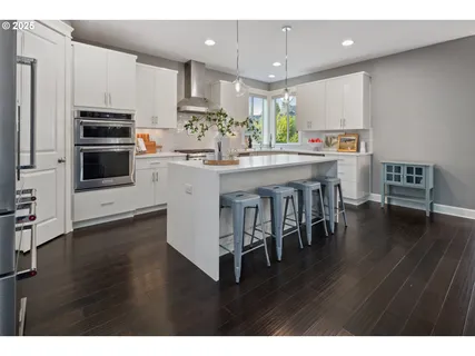 a kitchen with stainless steel appliances kitchen island granite countertop a stove a refrigerator a sink a dining table and chairs with wooden floor