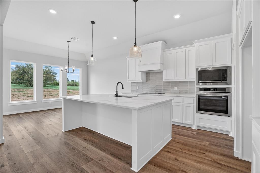 317 Skeen Peak Springtown, TX 76082 - Photo 4 of 31 Open-concept kitchen featuring a white center island with a sink, white cabinetry, integrated stainless steel appliances, a light-toned tile backsplash, and wood-finish flooring
