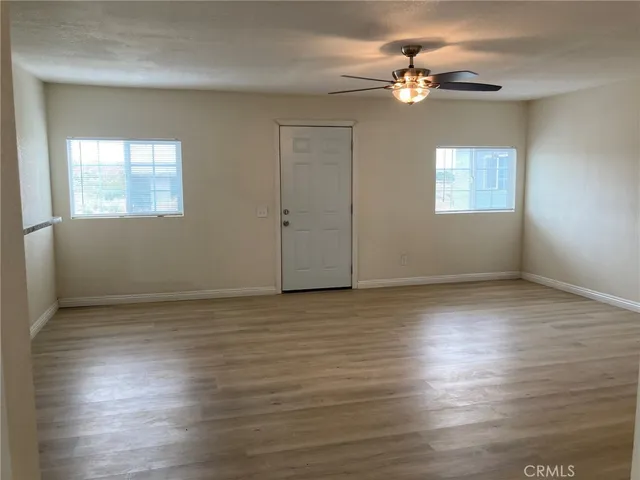 an empty room with wooden floor chandelier fan and windows