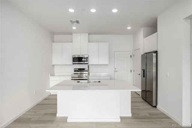 a large kitchen with stainless steel appliances a refrigerator a sink dishwasher and a stove with wooden floor