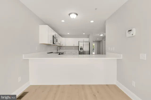 a view of kitchen with kitchen island white cabinetry a sink and a refrigerator