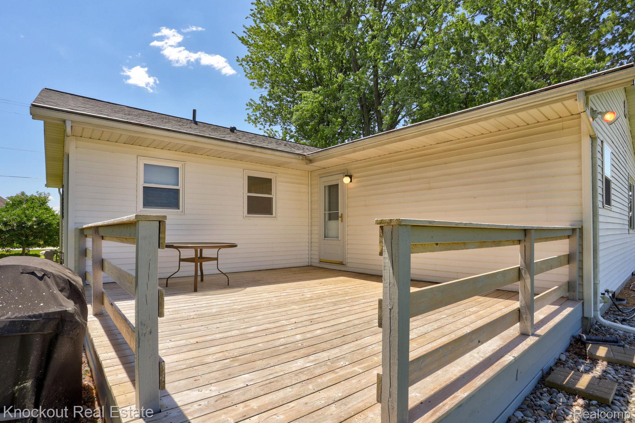 9941 Lange Road Birch Run, MI 48415 - Photo 34 of 42 Expansive wood deck with wood railings, featuring two exterior wall sconces and access to the home via a white screen door
