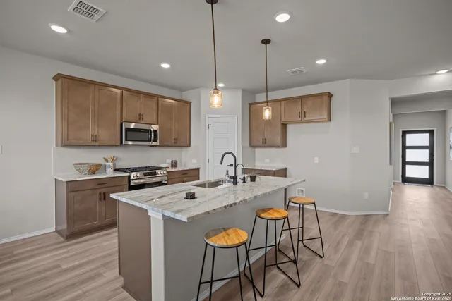 a kitchen with stainless steel appliances granite countertop a stove top oven a sink a dining table and chairs with wooden floor