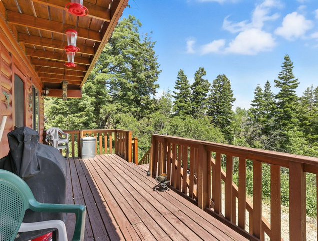 Expansive outdoor deck with wood-finish railing, wood-finish flooring, and a natural tree-lined backdrop