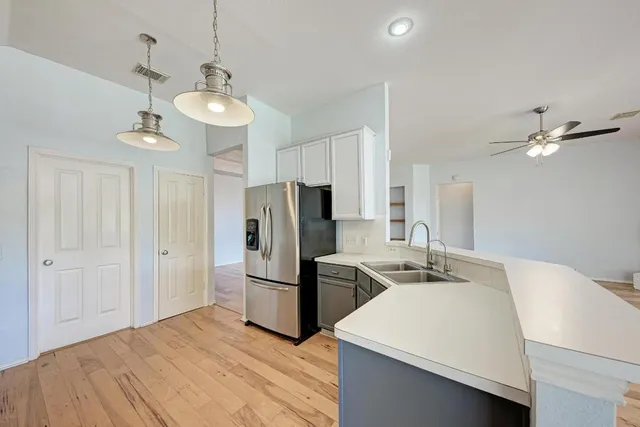 a kitchen with stainless steel appliances granite countertop a refrigerator a sink dishwasher a stove and white countertops with wooden floor