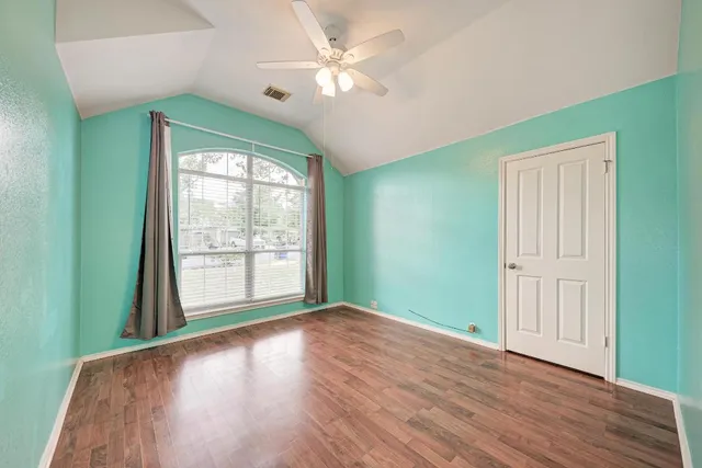 an empty room with wooden floor fan and windows