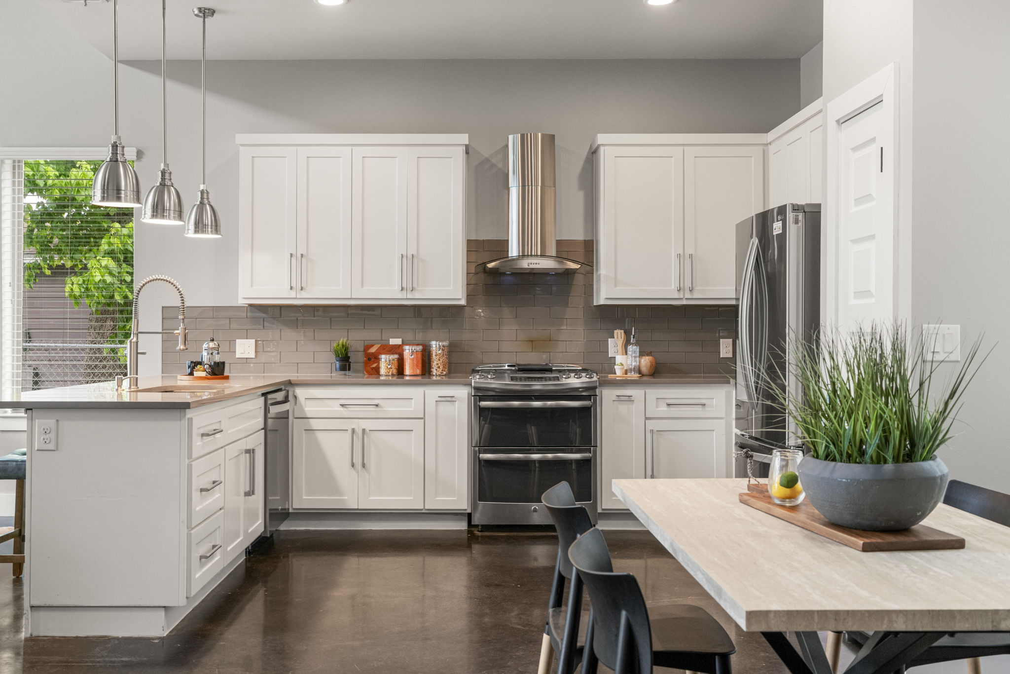 5204 Samuel Huston Avenue, Unit A Austin, TX 78721 - Photo 13 of 38 Contemporary kitchen featuring white cabinetry, a stainless steel appliance suite, a central island with a sink, pendant lighting, stained concrete flooring