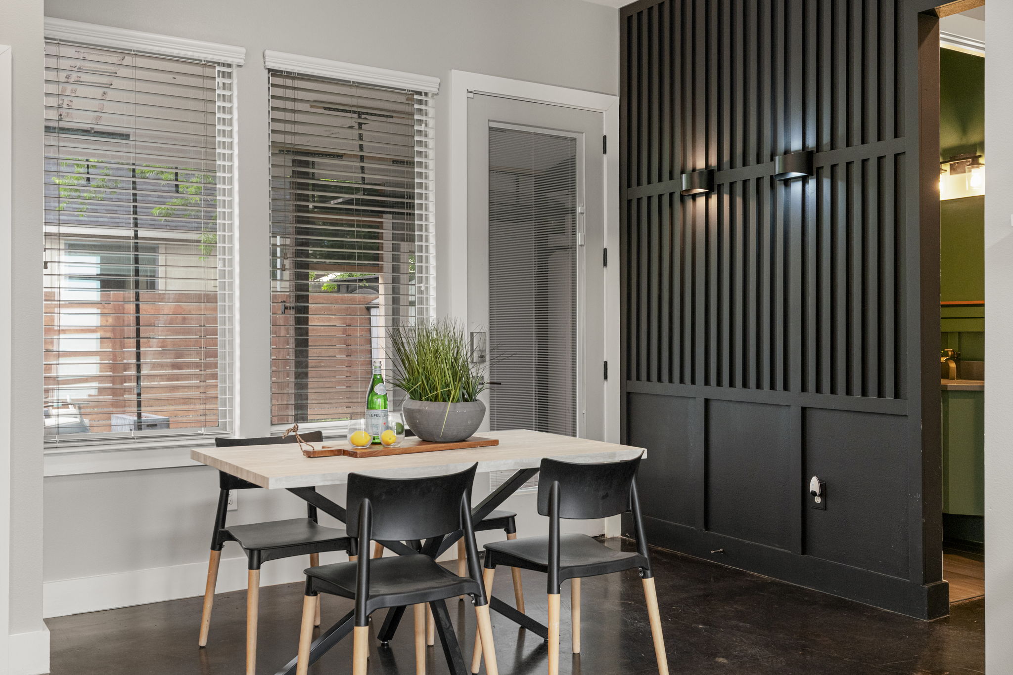 5204 Samuel Huston Avenue, Unit A Austin, TX 78721 - Photo 17 of 38 Dining area featuring a light-toned tabletop with contrasting dark chairs, wood-finish flooring, two large windows with blinds, a modern black slatted architectural partition, and integrated wall sconces