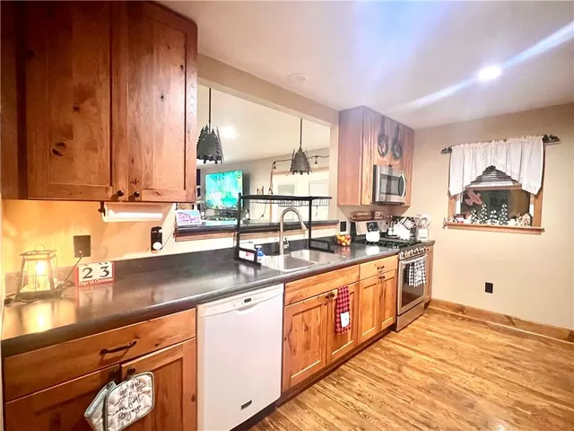 a kitchen with stainless steel appliances a sink dishwasher a stove and white cabinets with wooden floor