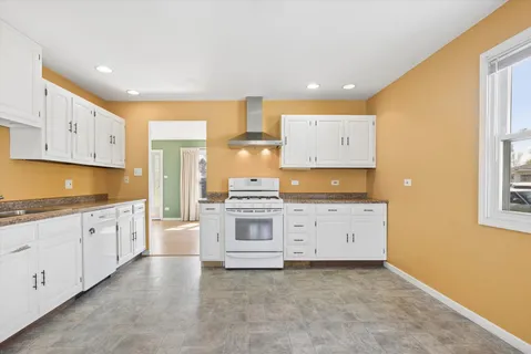 a large kitchen with granite countertop a stove a sink a window and white cabinets