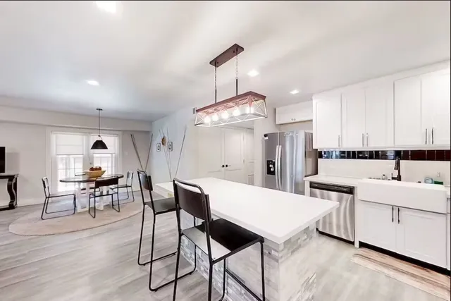 a kitchen with stainless steel appliances kitchen island granite countertop a refrigerator a stove a dining table and chairs with wooden floor