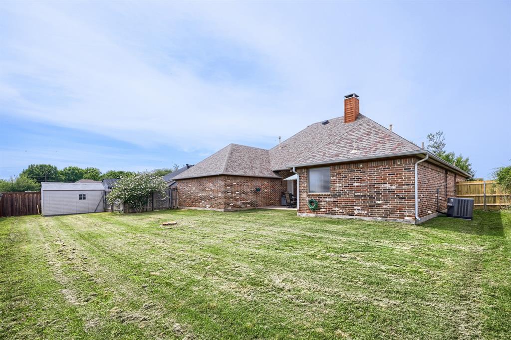603 Ash Street Pilot Point, TX 76258 - Photo 27 of 28 Expansive backyard featuring a manicured lawn, brick exterior, shingled roofing, a detached storage shed, and perimeter fencing