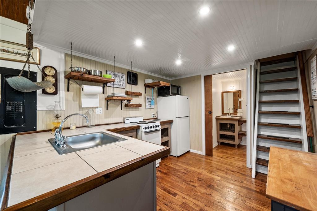 14036 Old Texaco Road Conroe, TX 77302 - Photo 21 of 40 Kitchen featuring a sink, open shelves, tile counters, wood finished floors, and white appliances