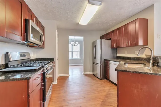 a kitchen with stainless steel appliances granite countertop a stove top oven a refrigerator a sink and dishwasher with wooden floor