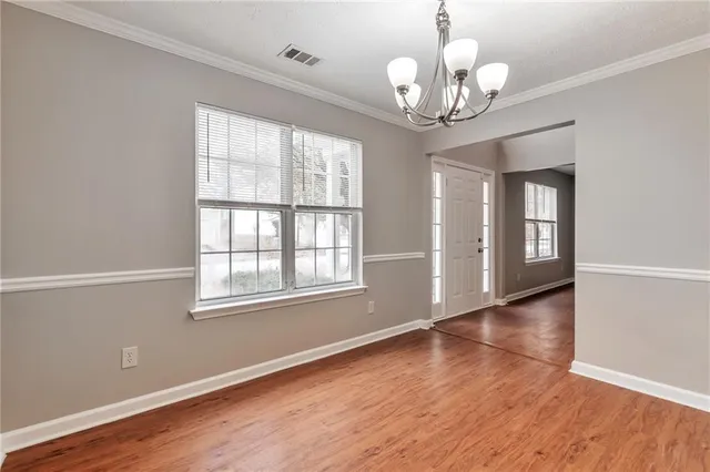 an empty room with wooden floor chandelier and windows